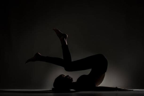 适合芭蕾舞女孩躺着和伸展练习瑜伽姿势。侧面点燃剪影对黑暗的背景…图片下载