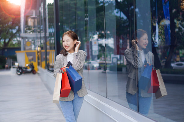 节日购物结束后，一位拎着购物袋的快乐女性在购物中心前开心地微笑着。图片下载