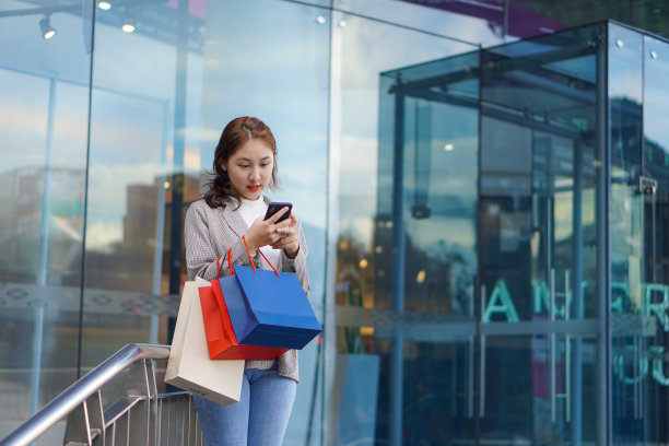 在购物中心前举行的“happy Smile Festival”上，一名拿着智能手机和购物袋的亚洲女性正在享受购物的乐趣。图片下载