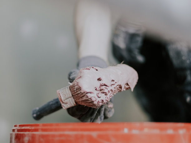 一个白人抹灰手拿着一个大刷子与红色硬化砂浆在一个桶图片下载