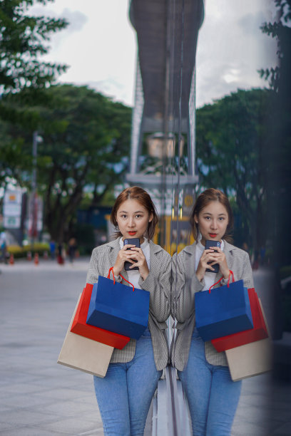 在购物中心前举行的“happy Smile Festival”上，一名拿着智能手机和购物袋的亚洲女性正在享受购物的乐趣。图片下载