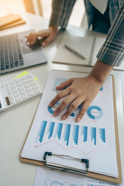 商人手里拿着笔，用图表工作，分析商业策略。财务统计用笔记本电脑坐在书桌上垂直查看图片下载