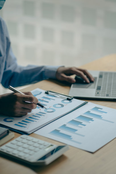 商人手里拿着笔，用图表工作，分析商业策略。财务统计用笔记本电脑坐在书桌上垂直查看图片下载