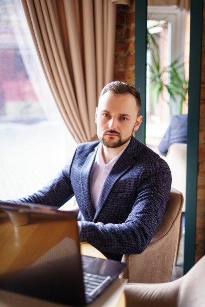 一个留着胡子的年轻人坐在餐馆的桌子旁。图片下载