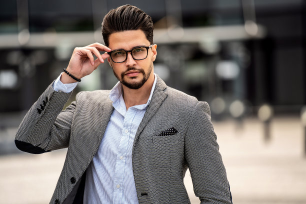 英俊潇洒的年轻男子戴着时髦的眼镜，看着镜头，在户外摆姿势。商人。图片下载