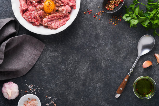 生肉馅。碎肉牛肉，猪肉或羊肉香料，香草和鸡蛋在黑色旧混凝土背景的白色盘子上。新鲜的肉末，随时可以煮。食物烹饪的背景。前视图。图片下载