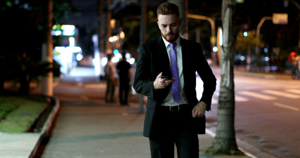 商人看着手机设备在晚上走在人行道上图片下载