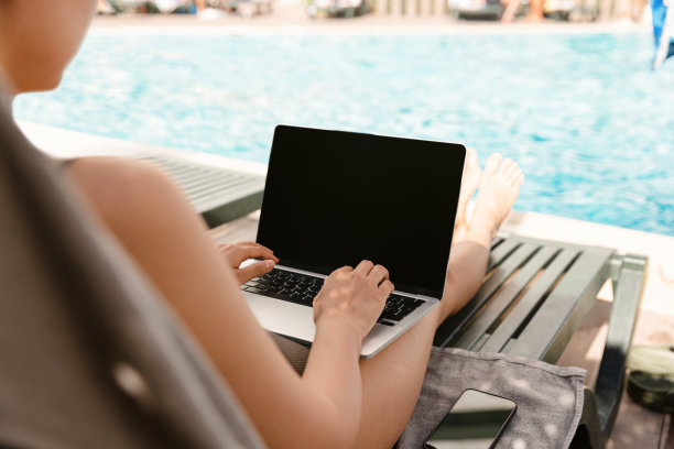 年轻女子在游泳池边喝着鸡尾酒边使用笔记本电脑图片下载