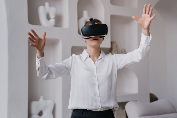 年轻的女学生穿着白衬衫和黑裤子，戴着vr眼镜在室内探索艺术和博物馆，靠墙站着，架子上放着陶瓷。女孩使用虚拟现实。教育和乐趣。图片下载