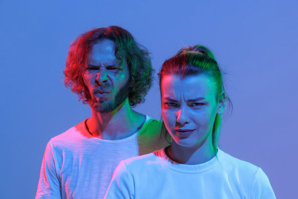 年轻的男人和女人的肖像在霓虹灯蓝色背景孤立。不愉快的表情。不喜欢图片下载