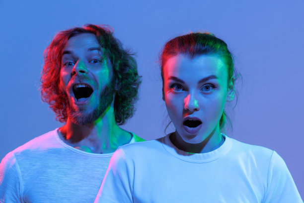 年轻的男人和女人的肖像在霓虹灯蓝色背景孤立。震惊的情绪图片下载
