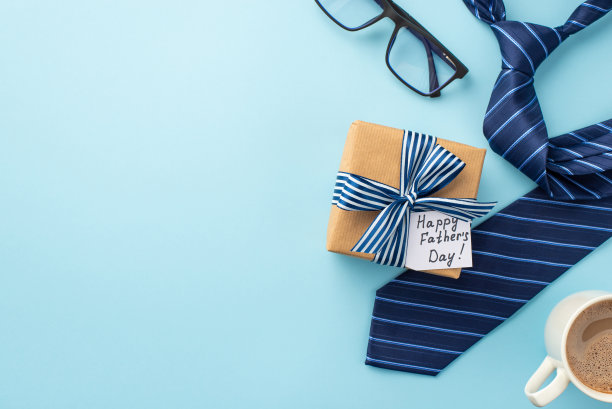父亲节的概念。顶视图照片的牛皮纸礼品盒与缎带蝴蝶结和明信片杯咖啡杯和蓝色领带上孤立粉彩蓝色背景与空白图片下载