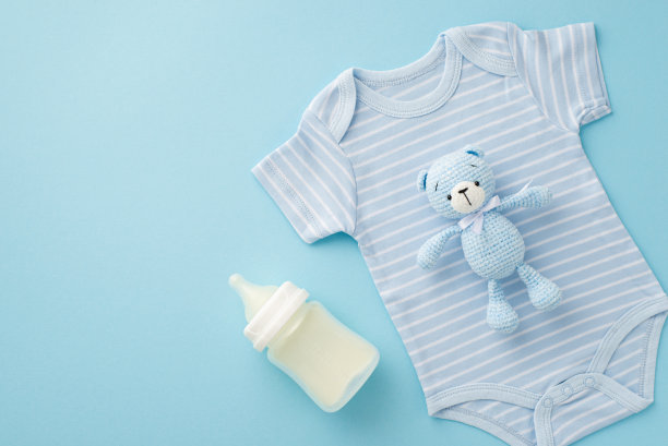 小配件的概念。俯视照片的蓝色紧身衣针织泰迪熊玩具和奶瓶孤立粉彩蓝色背景图片下载