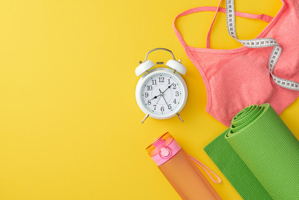 健康的概念。顶视图照片的粉红色运动胸罩瓶的水绿色运动垫卷尺和闹钟上孤立的黄色背景图片下载