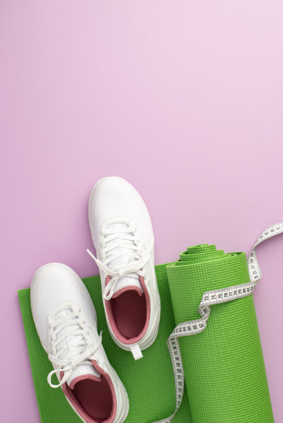 减肥的概念。俯视图垂直的照片，白色运动鞋和卷尺在绿色运动垫子上孤立的淡紫色背景与copyspace图片下载