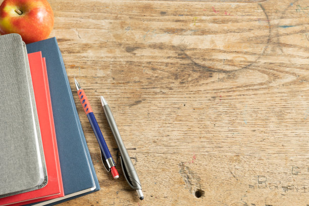 木桌上有一堆灰、红、蓝的书，还有苹果和笔图片下载