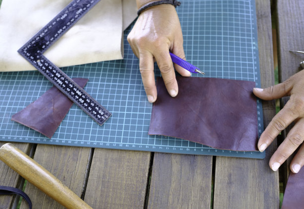 在一个小手工场里，一个手艺人正在用她的双手制作一个皮包。图片下载