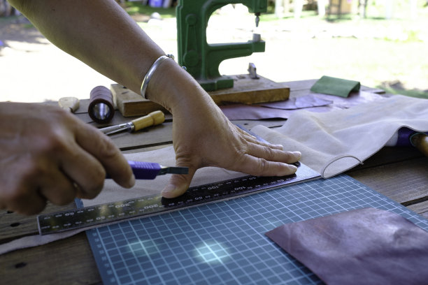 在一个小手工场里，一个手艺人正在用她的双手制作一个皮包。图片下载