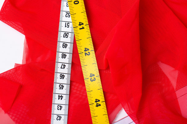 在白色的桌子上缝纫配件。剪刀、卷尺、布、布、红胶带。图片下载