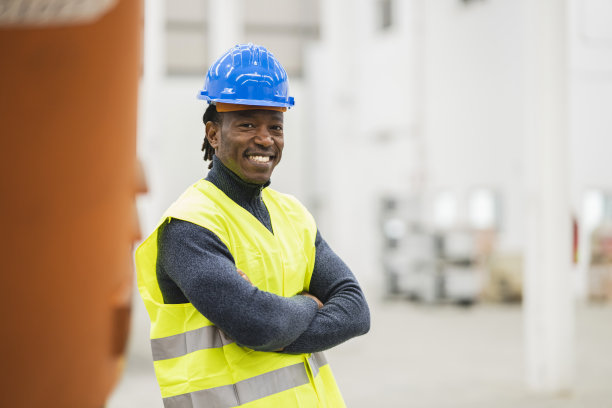 一名非洲籍物流工人戴着头盔，身穿反光背心，双臂交叉微笑着图片下载