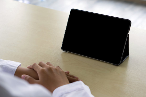 后视图的女人在白色长袍使用一个空白屏幕平板，而坐在木桌。图片下载