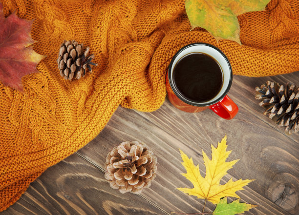 秋季构图格纹橘色，红色的咖啡杯，黄色的树叶和松果，背景是木制的。素材图片
