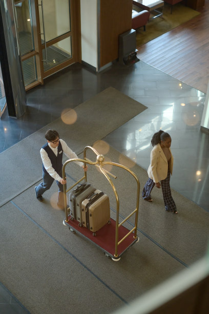 身穿行李员制服的年轻人推着行李车为客人送行图片下载