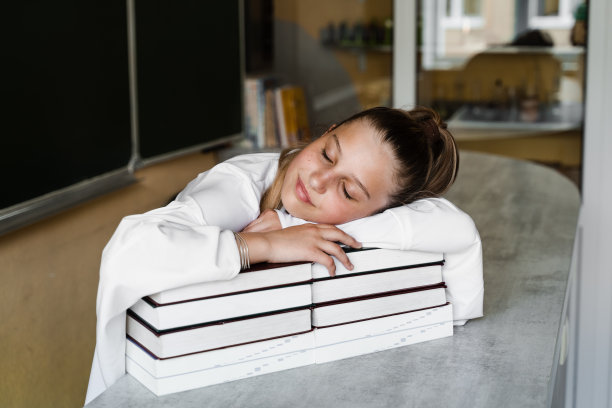 疲惫的女生躺在学校的黑板上睡觉。学校教育。这个女孩对教家庭作业感到厌倦。图片下载