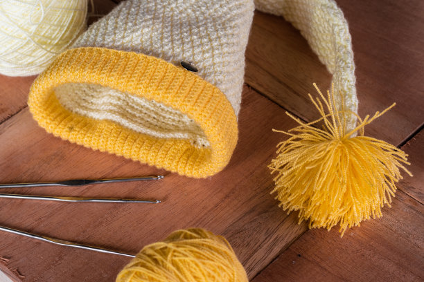 静物精灵的一顶黄色的帽子用钩针编织而成，用于服装的设计和编织，放在一个木制的背景上。一卷卷的羊毛和钢编织针。图片下载