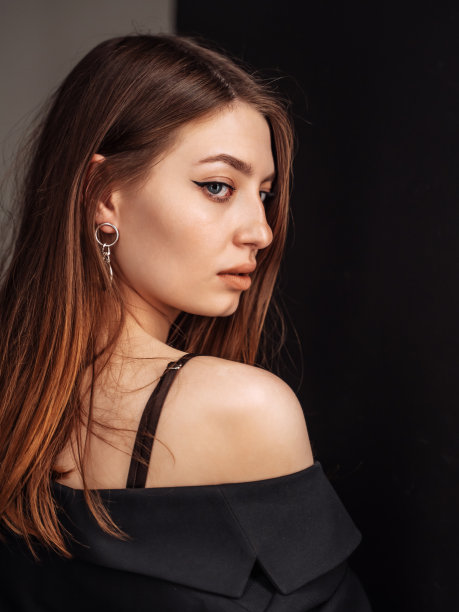 时尚风格。时尚美女在性感的衣服显示回来看后面，看着相机。长发造型的女士在现代黑色墙壁后摆造型。图片下载