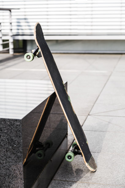 在写字楼附近的现代城市街道上，破旧的绿色轮子的滑板独自靠在黑色花岗岩的支架或座位上图片下载