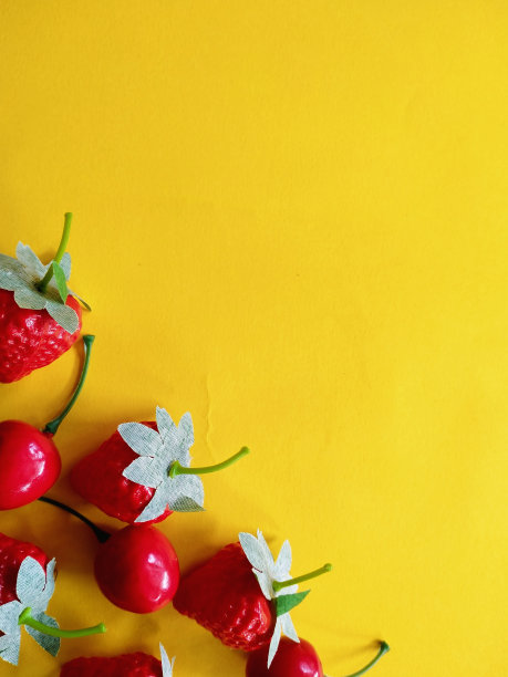 黄色底色的假草莓和樱桃。免费空间图片下载