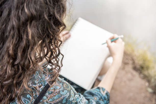 穿着裙子的白人女孩坐在河边的地上，在素描本上画画图片下载