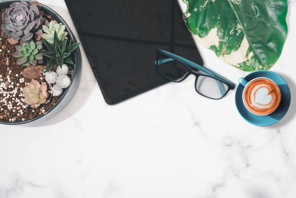 平铺，俯视图办公桌书桌。工作空间，平板电脑，办公用品，绿叶，和咖啡杯在白色背景，复制空间的文本。图片下载