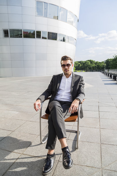穿着黑色西装的男性商人或工人坐在现代建筑旁的椅子上图片下载