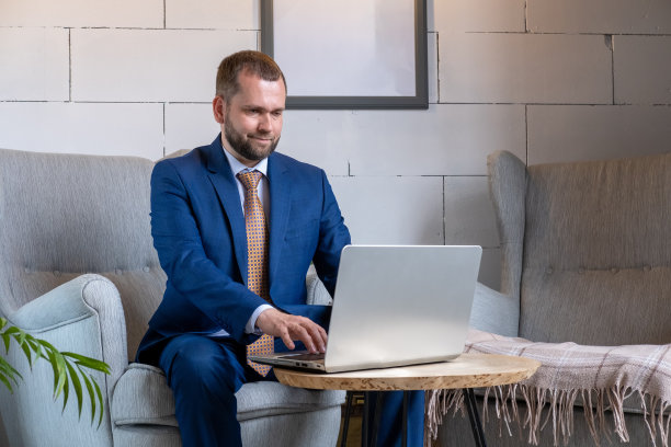 穿着蓝色西装、留着胡子的中年男子在咖啡馆用笔记本电脑。在工作场所用笔记本电脑工作的英俊男性自由职业者图片下载