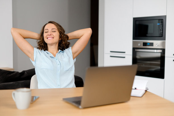白人成功女性坐在舒适的椅子上，微笑着，在忙碌的一天后放松地坐在桌子上，手放在脑后图片下载