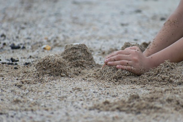 晚上在沙滩上玩沙子的孩子的手的照片，展示了教育、自我发展、创造力和成长。图片下载