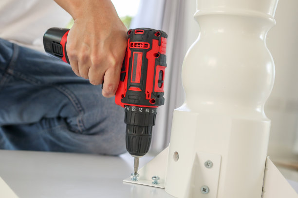 一名男子在家用无线螺丝刀组装白色餐桌家具图片下载