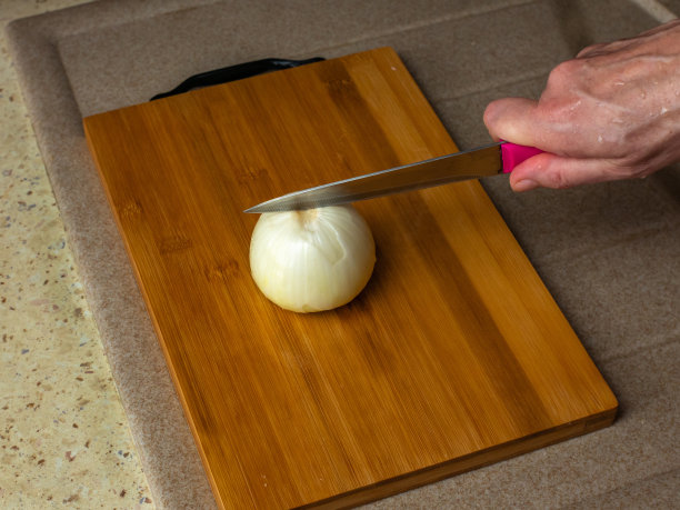 特写女性的手在木板上用刀切洋葱。图片下载
