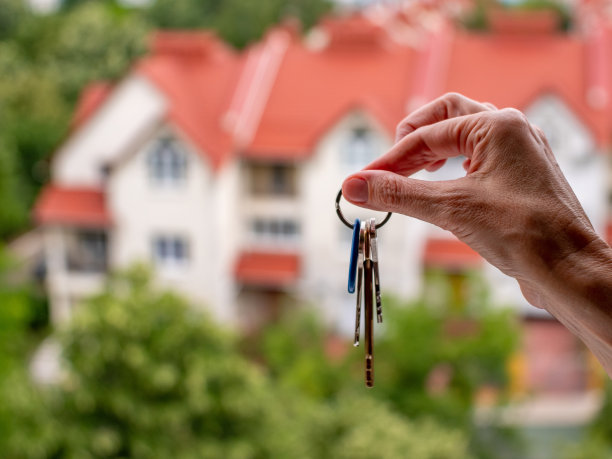 一个女人的手握着公寓的钥匙，背景是美丽的住宅楼。图片下载