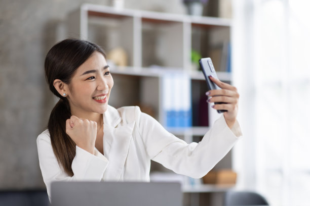 一个快乐的亚洲女人用智能手机和笔记本电脑的照片，微笑着坐着图片下载