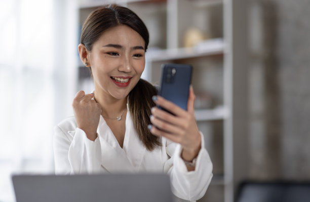 一个快乐的亚洲女人用智能手机和笔记本电脑的照片，微笑着坐着图片下载