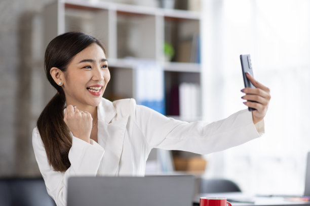 一个快乐的亚洲女人用智能手机和笔记本电脑的照片，微笑着坐着图片下载