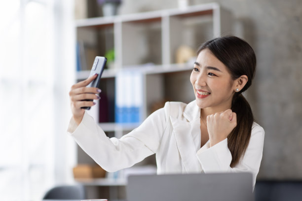 一个快乐的亚洲女人用智能手机和笔记本电脑的照片，微笑着坐着图片下载