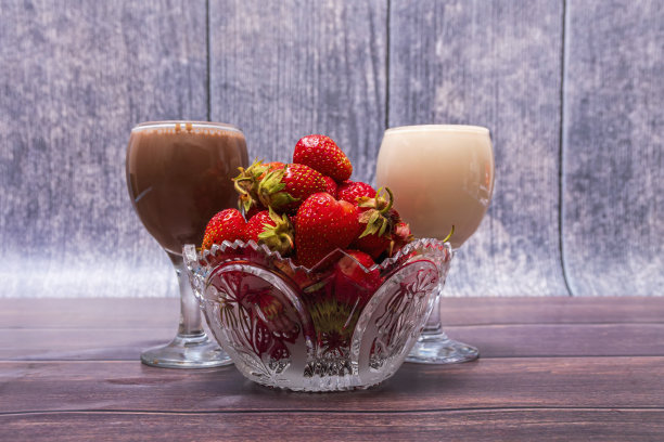 水晶花瓶和成熟的红色草莓和两杯鸡尾酒站在木桌上。图片下载