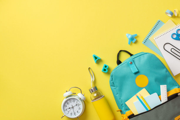 回到学校概念。俯视图照片的背包闹钟铅笔记事本瓶子字母胶带剪刀和平面形状的卷笔刀孤立的黄色背景与copyspace图片下载
