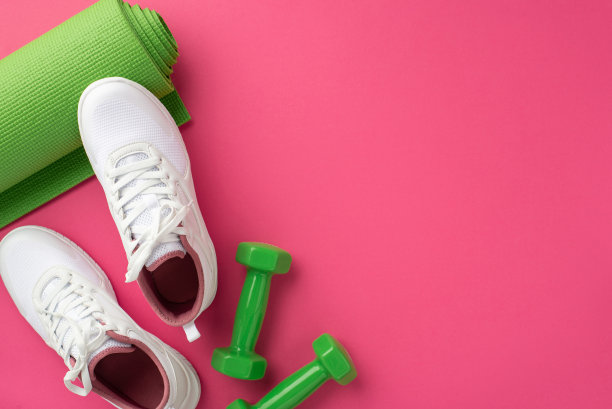 健身器材的概念。俯视图照片的绿色瑜伽垫哑铃和白色运动鞋在孤立的粉红色背景图片下载
