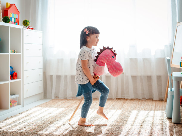 在育儿室里，小女孩骑着马鞭又跳又跑。图片下载