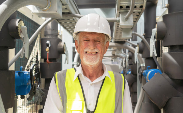 年老的工程师或工人，在工业工厂工作的人。屋顶建筑上的冷却塔。系统工作的机器。冷凝器供水管路。通风式压缩机图片下载